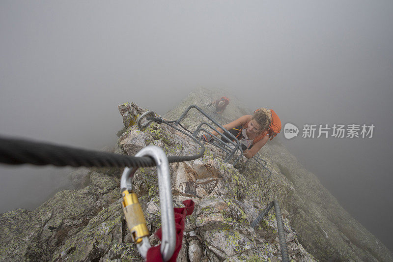 在雾中，一名年轻女子爬上via ferrata